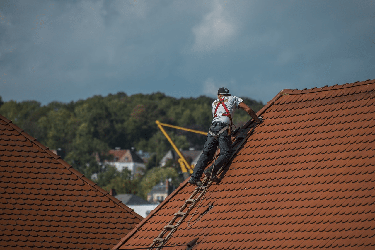 roofer standing on a roofing ladder repairing shingles