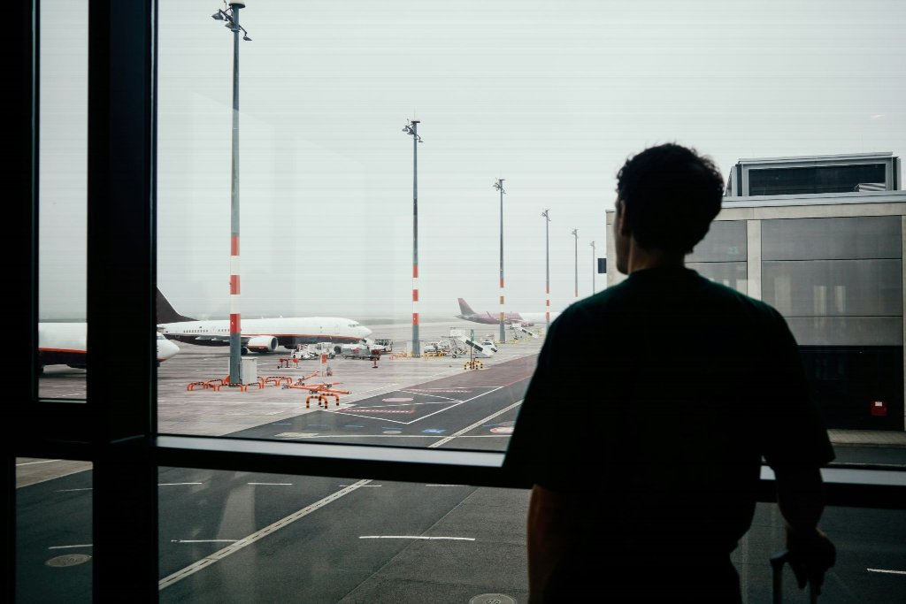 person looking out the window at an airport - Who Helps When a Loved One Passes Away Overseas